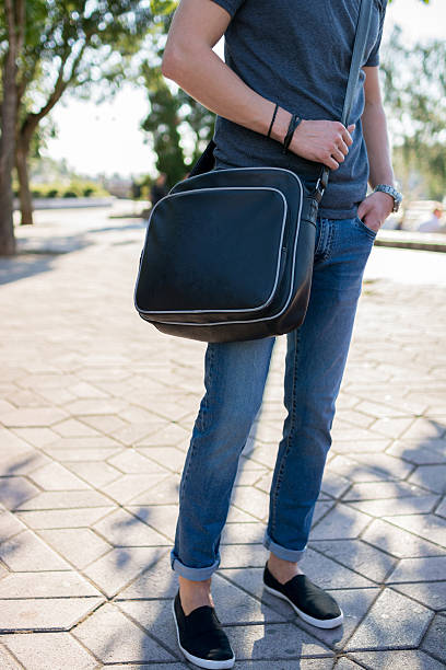 Stylish man with a bag posing in city park stock photo