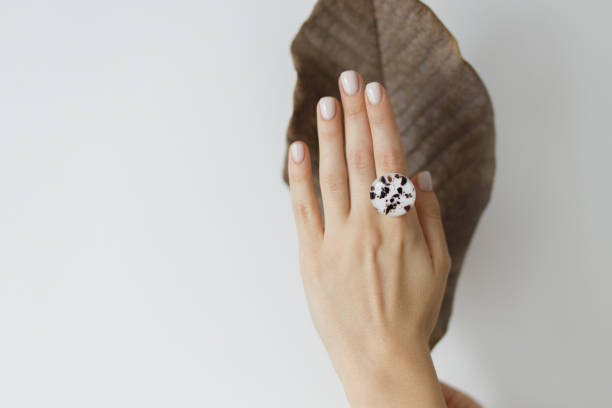 Stylish modern round ring on beautiful hand on background of brown dried big leaf on white wall stock photo