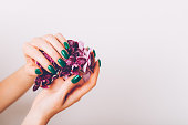 Stylish trendy purple female manicure. Woman hands are holding orchid flowers