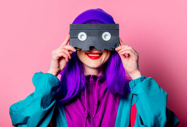 Stylish white girl with purple hair, 80s tracksuit hold video tape stock photo