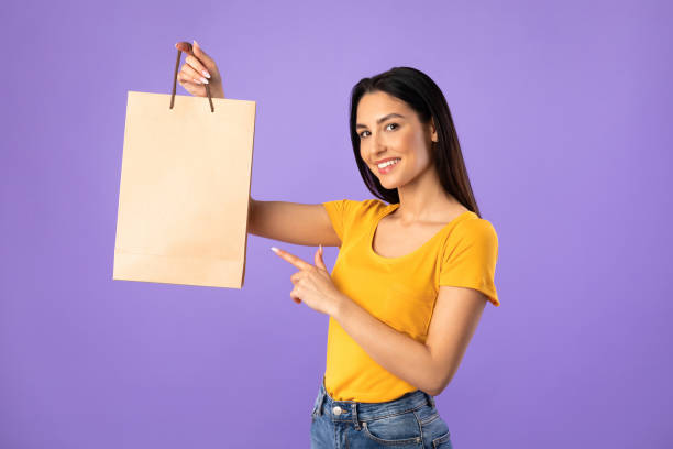 stylish woman pointing at paper shopping bag - paper bag craft imagens e fotografias de stock