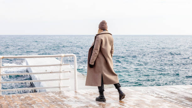 Stylish woman standing alone at the sea in winter stock photo