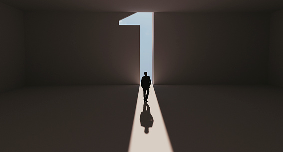 Man walks towards a big number one symbol that lights up. He is surrounded by darkness, but walks on a path of sunshine reaching first place. Note: Digitally generated image.