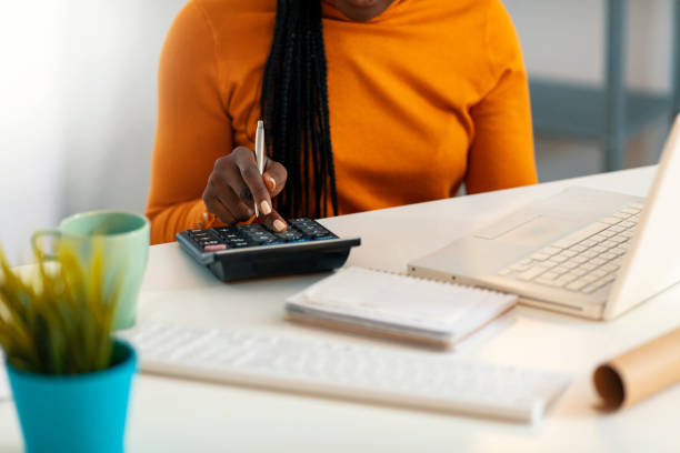 Success is in the hands of productive people Photo of one Attractive African-American young woman working at desk with laptop and calculator - taking notes. calculator stock pictures, royalty-free photos & images