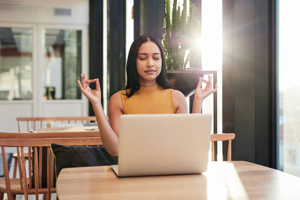 Success starts with good intention Shot of a young businesswoman meditating while using a laptop in a modern office mindfulness stock pictures, royalty-free photos & images