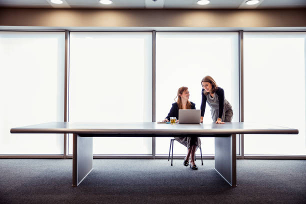 Successful and Confident Businesswomen Two woman at a large table discussing business with a laptop in from of them. They look positive and confident. They are in a large room wide stock pictures, royalty-free photos & images