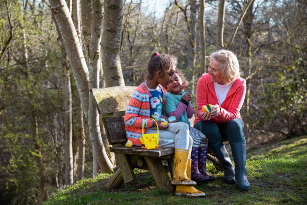 Successful Easter Egg Hunt! A grandmother and her two young granddaughters sitting on a wooden bench in a woodland area in Hexham, Northumberland. They have collected easter eggs on an Easter egg hunt, they have their baskets and they're looking at all the eggs they've found. easter sunday stock pictures, royalty-free photos & images