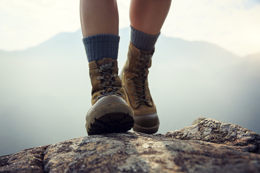 Suceesful woman hiker legs stand on mountain peak cliff edge