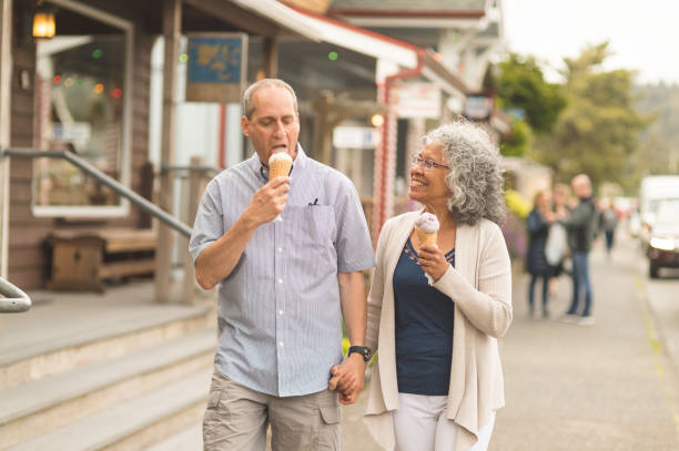 A summer afternoon together... A senior couple enjoy a walk together and ice cream cones on a lovely summer afternoon. They are passing by several small businesses in a small downtown district. She is looking at him with love...or maybe looking at his ice cream. small town stock pictures, royalty-free photos & images