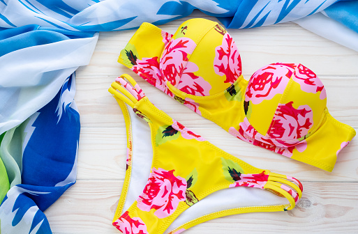 Summer background with fashion beachwear, yellow bikini and blue pareo on a wooden background. The concept of sea recreation, leisure. Swimsuit with floral print. Women's swimming suit