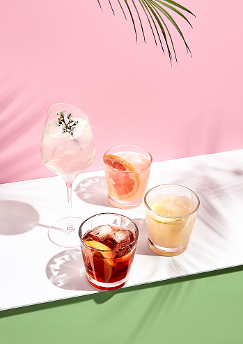 Summer cocktail with fruit and ice. Drink on white table over pink wall in sunlight with palm leaf shadow. Summer, tropical, fresh cocktail concept.