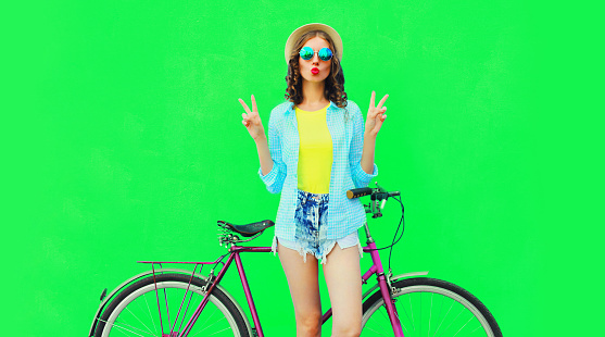 Summer colorful image of happy young woman with bicycle on vivid green background