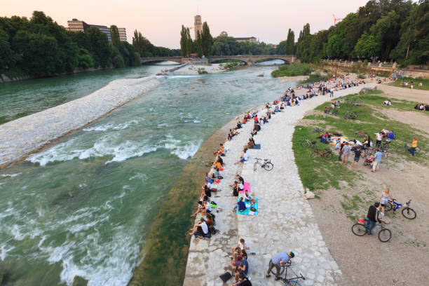 Summer evening at river Isar, Munich Munich, Germany - July 10, 2013: A summer evening at river Isar in Munich. Several locals and tourists are enjoying the warm evening at the shore of lake Isar within Munich, Germany. Some of them are having a picnic or a drink. In the background to the left the European Patent Office and to the middle the German Museum the worlds largest museum of technology and science. river isar stock pictures, royalty-free photos & images