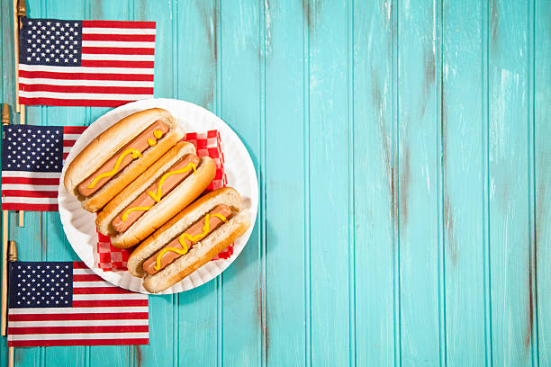 Summer holiday picnic. Hot dogs, USA flags. Blue wooden table. Happy Independence Day America!  Three USA flags form a left side border with hot dogs on white plate. Copyspace to right. Teal blue wooden beadboard background with grunge painted effects.  Memorial Day, July 4th, Veteran's Day, Labor Day, Flag Day summer picnic concepts.  American pride and patriotism. memorial day background stock pictures, royalty-free photos & images