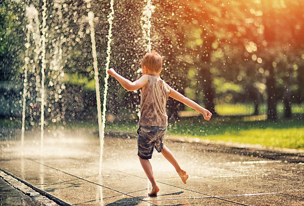 Summer in the city - little boy playing with fountain Hot summer day in the city. Little boy is having fun playing in the park fountain. He is running barefeet getting wet and splashing. fountain stock pictures, royalty-free photos & images