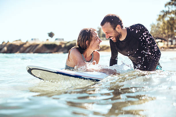 Summer love Loving couple of smiling surfers in the water, flirting while waiting for a good wave to come beach holiday stock pictures, royalty-free photos & images