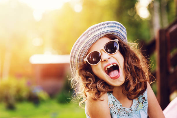 summer portrait of happy kid girl on vacation in sunglasses and hat, laugh and showing tongue. stock photo
