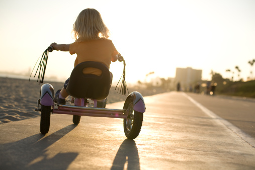 A young girl rides her tricycle towards sunset at Long Beach, Ca.