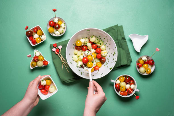 Summer salad with tomatoes and mozzarella. Serving Caprese salad Salad with cherry tomatoes and mozzarella balls on green background. Above view of woman serving caprese salad. Summer salad portions. Healthy eating. aqua menthe photos stock pictures, royalty-free photos & images