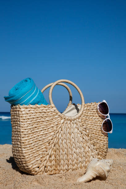 Summer straw bag with blue towel and sunglasses on a tropical sandy beach stock photo