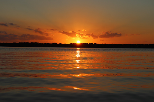 Amber colored sunbeams across the sky reflecting warm hues in the water to the horizon.