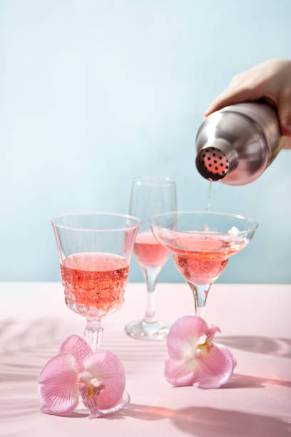 Summer tropical pink cocktail wine champagne in a different glasses decorated pink orchid flowers. Human hand pouring from shaker cocktail stock photo