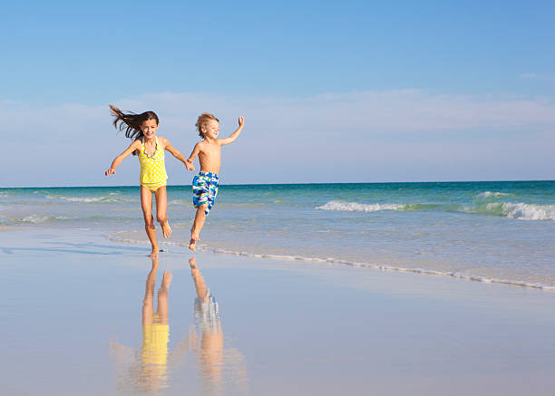 Summer Vacation Two children having an awesome time running along the beach shore. skipping stock pictures, royalty-free photos & images