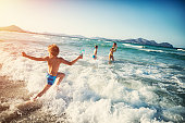 Three kids - a girl and two boys  - are having fun in sea.  Little boy is running and jumping in the sea, his brother and sister already standing in the sea.