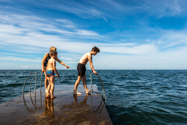 Summer view of a family on a stone jetty about to  swim in the ocean of the Baltic Sea with blue sky and horizon. stock photo
