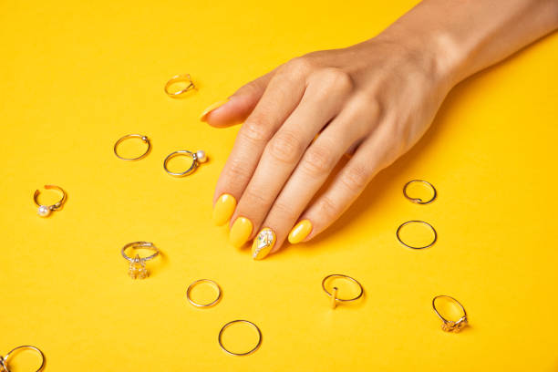 Summer yellow manicure with crystals and jewelry ring Summer yellow manicure with crystals and jewelry ring. Female hand with nails design on a green monstera leaf gold ring on finger stock pictures, royalty-free photos & images