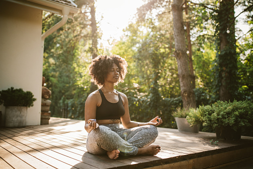 Young woman practicing yoga outdoors on porch, she enjoy in summer sun and meditation