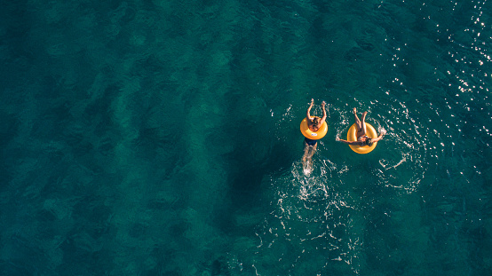 High angle view photo of a two young women relaxing while floating in the ocean using swimming tubes; wide photo dimensions