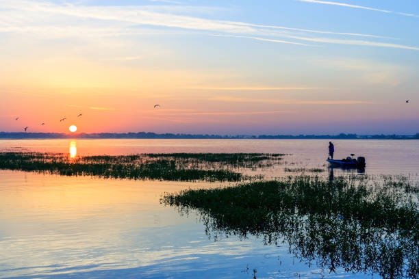 Sun Rising over this Lone fisherman in his fishing boat on Lake Tohopekaliga - a nationally famous Bass Fishing Lake - He is just off the shore at Kissimmee, Florida stock photo