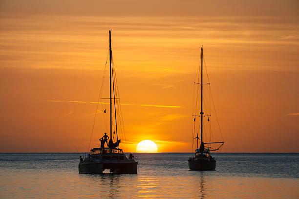 Sun setting over ocean, person standing on sailboat in silhouette Large white sun on horizon in Caribbean. Marigot Bay St Lucia. catamaran stock pictures, royalty-free photos & images
