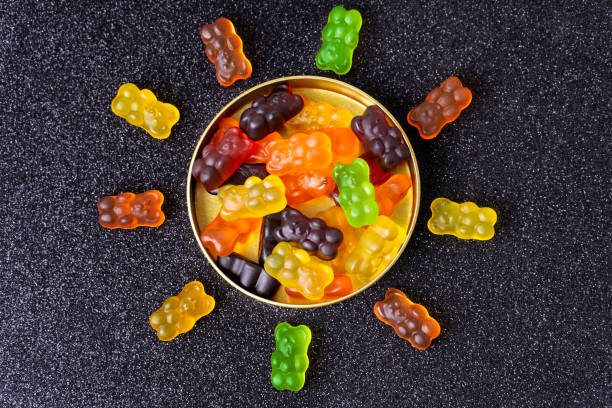 Sun symbol made of multicolored gummy bears Gummy bears arranged in the shape of a sun around a candy box on a sugar coated background. teddy ray stock pictures, royalty-free photos & images