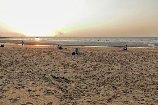 Sunset over Mindil Beach at low tide located in The Gardens suburb facing northwest on Fannie Bay-incidental people in the image. Darwin-Northern Territory-Australia.
