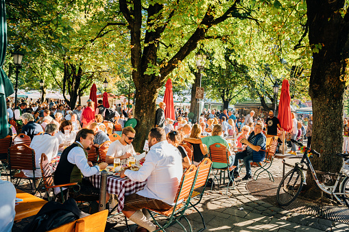 Munich, Germany - September 29, 2016: Viktualienmarkt beer garden is located at Munich's central food market. People sitting at the wooden tables and enjoying the sunny weather. They are drinking Beer and eating traditional Bavarian meals.
