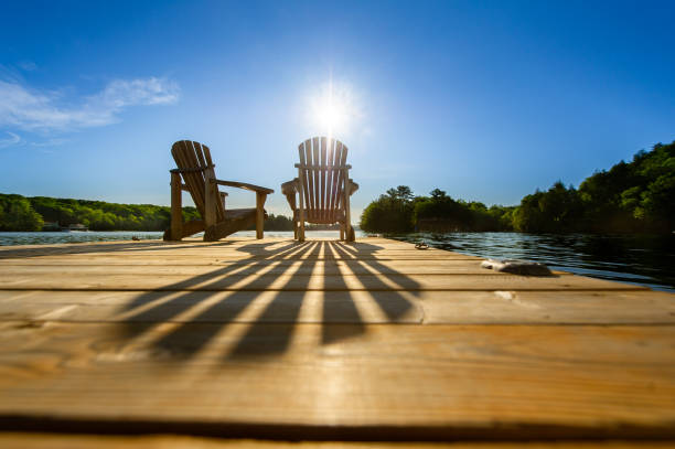 Sunrise on two empty Adirondack chairs sitting on a dock stock photo