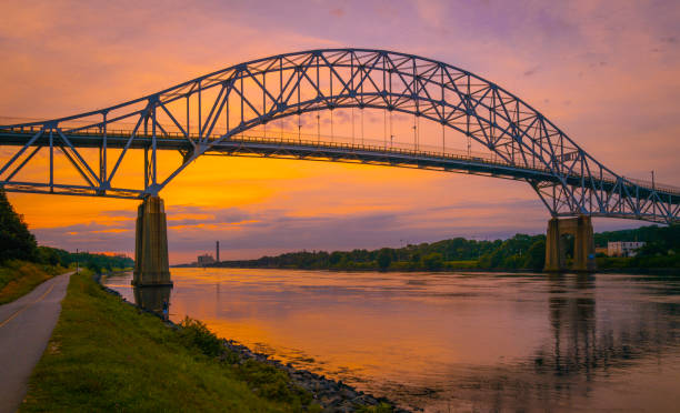 Sunrise over the arching Sagamore Bridge and riverbank footpath in Cape Cod Canal stock photo