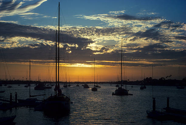 Sunset and clouds over moored yachts Vibrant sunset with backlit clouds over moored yachts in the bay at Newport Beach, California. hearkencreative stock pictures, royalty-free photos & images