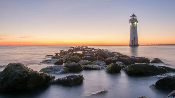 Sunset at New Brighton Lighthouse - Wirral The tide going out at New Brighton beach revealing the rocky shoreline and base of the lighthouse the wirral stock pictures, royalty-free photos & images