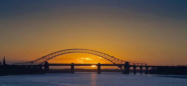 Sunset behind the Runcorn Bridge Bridge over the river Mersey at Runcorn Cheshire, taken as the sun sets behind it, reflected in the river. Also known as the Silver Jubilee bridge cheshire england stock pictures, royalty-free photos & images