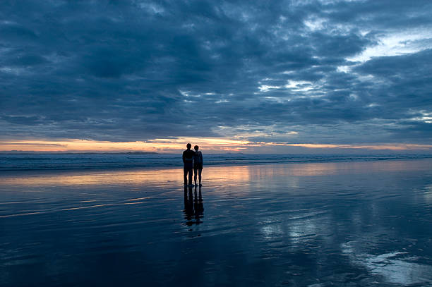Sunset Couple "A couple admire a dramatic sunset at Muruwai Beach. Auckland, New Zealand." divorce beach stock pictures, royalty-free photos & images