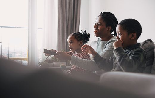 A portrait of a beautiful happy young African-American mother and her young boy and a girl watching tv in the living room while spending quality time together at home.
