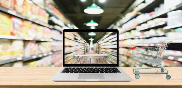 supermarket aisle blurred background with laptop computer and cart on wood table online shopping concept supermarket aisle blurred background with laptop computer and cart on wood table online shopping concept asian online grocery store stock pictures, royalty-free photos & images