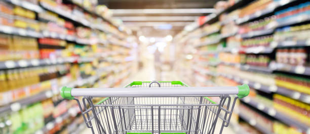 supermarket shelves aisle with empty shopping cart defocused interior blur bokeh light background supermarket shelves aisle with empty shopping cart defocused interior blur bokeh light background market retail space photos stock pictures, royalty-free photos & images
