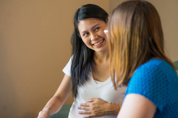 Support from a Doula Beautiful young pregnant woman of Malaysian ethnicity smiling at her midwife as they are sitting in her living room as they discuss her birth plan. She is in the third trimester of her pregnancy. midwife stock pictures, royalty-free photos & images