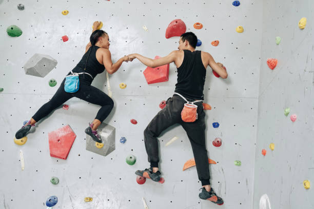 Supportive sportspeople climbing wall up Back view man and woman working out in team and hitting hands while hanging on wall in bouldering center bouldering stock pictures, royalty-free photos & images