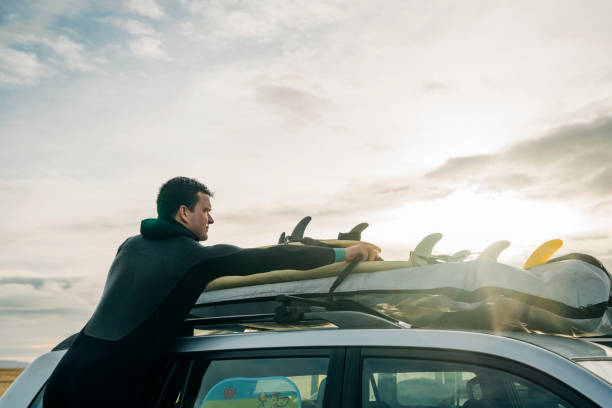 surfer lädt sein surfbrett auf auto - auto packen für den urlaub winter stock-fotos und bilder