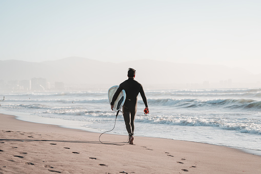 surfer walking on the beach with a surfboard getting into the ocean in La Serena, Chile